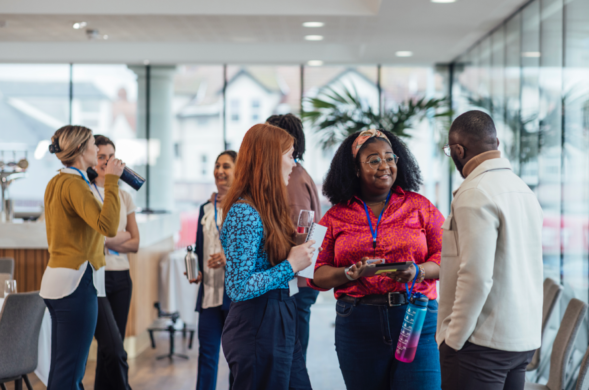 A group of diverse professionals chatting and networking at a modern industry event, with name badges and notepads in hand.
